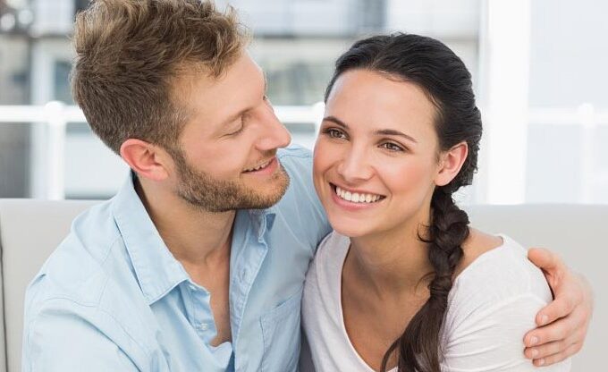 A man and woman sitting on the couch smiling.